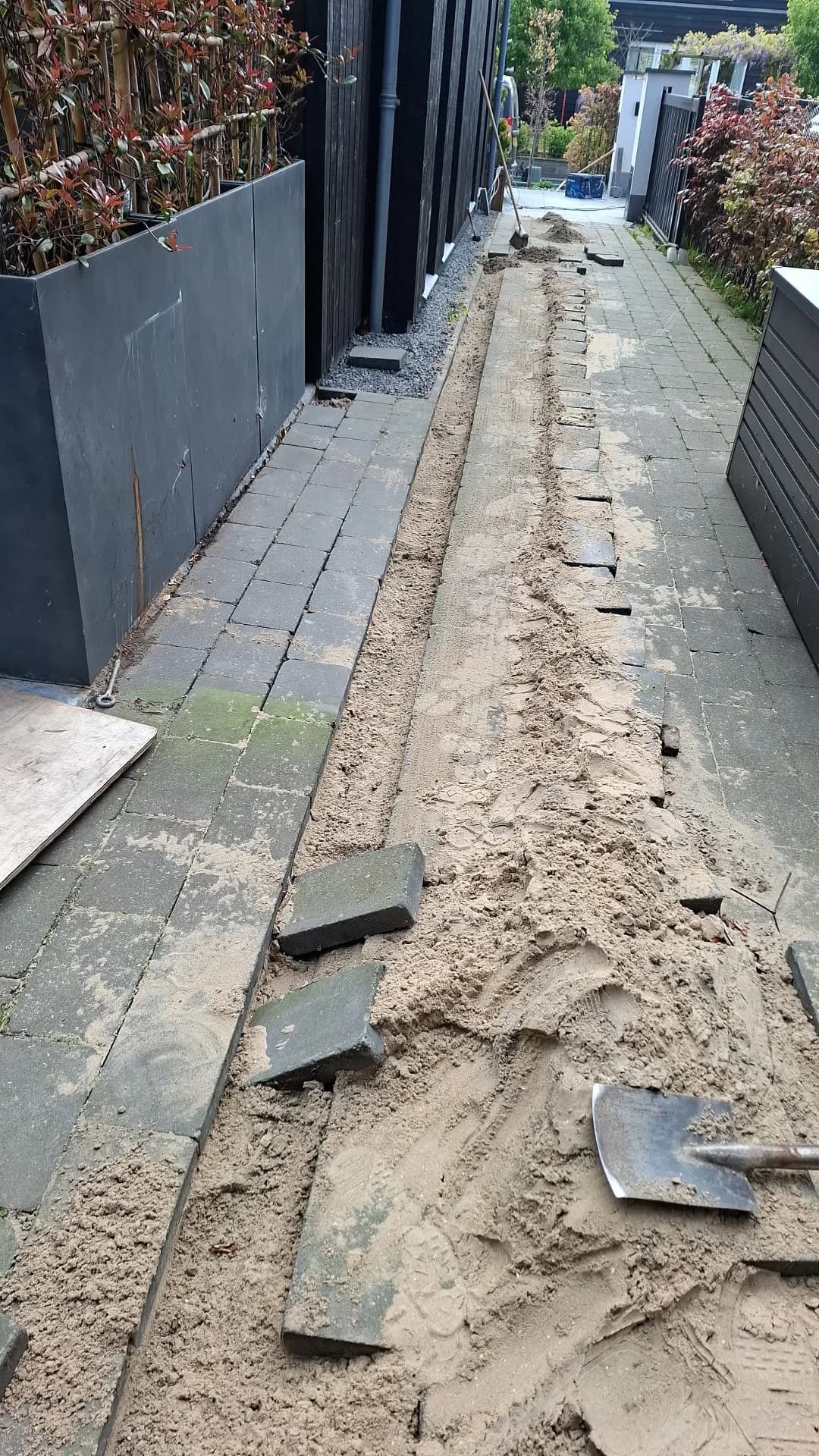 Opengebroken tuinpad met een kabelsleuf en tijdelijk verwijderde tegels tijdens de aanleg