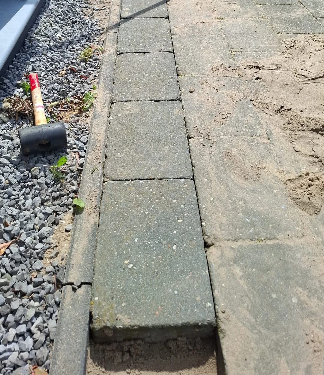 Betontegels op zand naast een grindstrook tijdens het terugleggen van het straatwerk