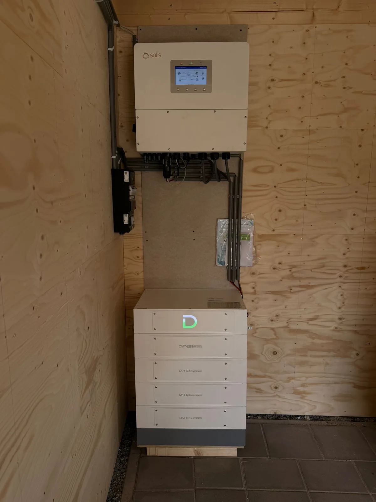 Solis omvormer met daaronder een Dyness thuisbatterij tegen een houten schuurwand, geplaatst door Maatje Solar Systems
