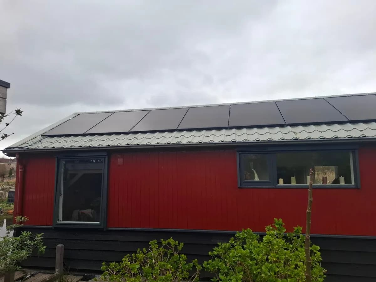 Zwarte zonnepanelen op het schuine dak van de rode woonboot