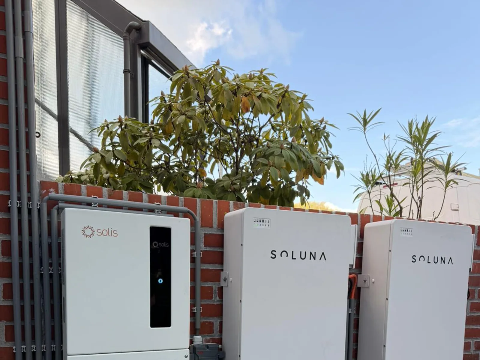 Solis omvormer en twee Soluna thuisbatterijen buiten gemonteerd tegen een lage bakstenen muur