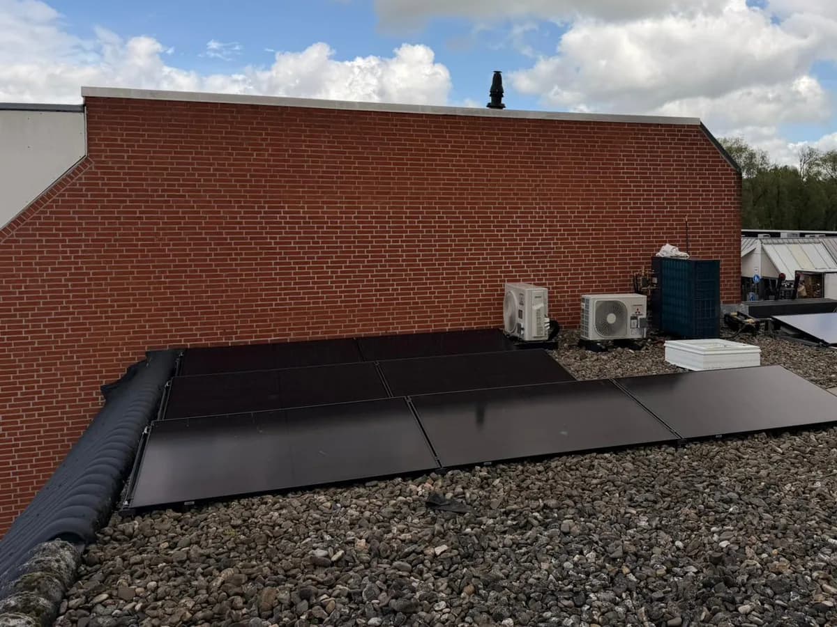 Plat dak met zwarte zonnepanelen tegen de bakstenen gevel van een woning in Zaandam